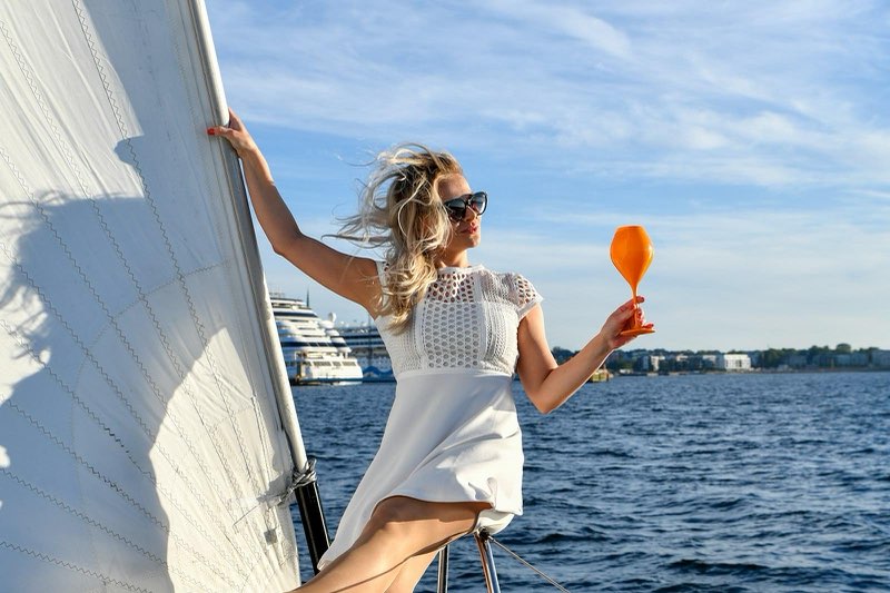 Two women in sunglasses, one holding an orange glass, on a sailboat.