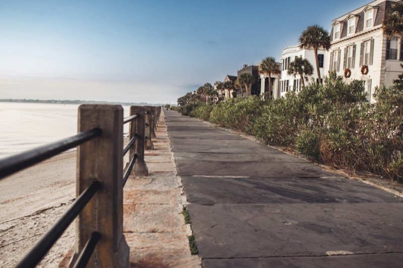 The flagstone Battery promenade and seawall at blue hour, historic houses and palmettos ahead.